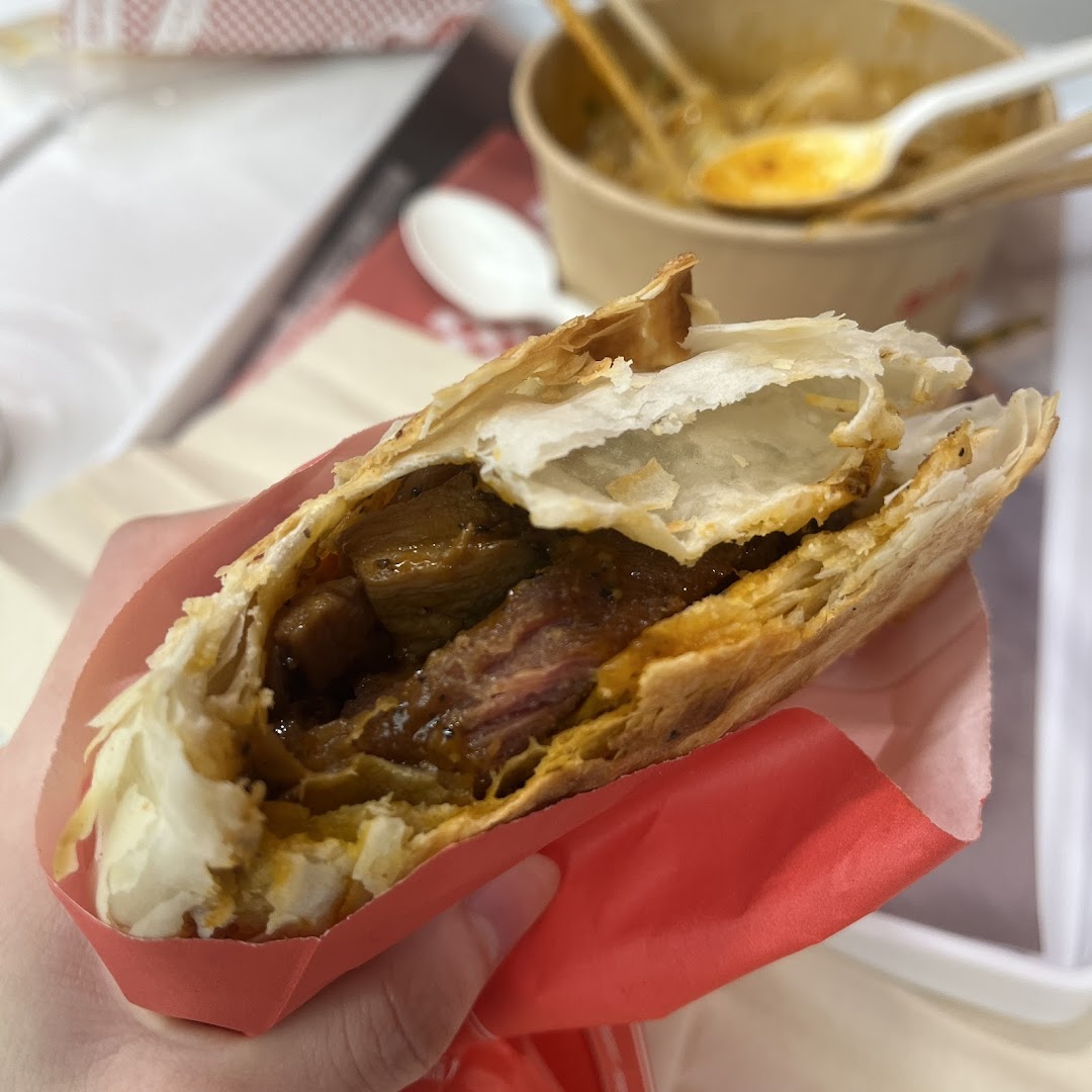 A hand holds a delicious roujiamo, showcasing its flaky pastry and savory meat filling.