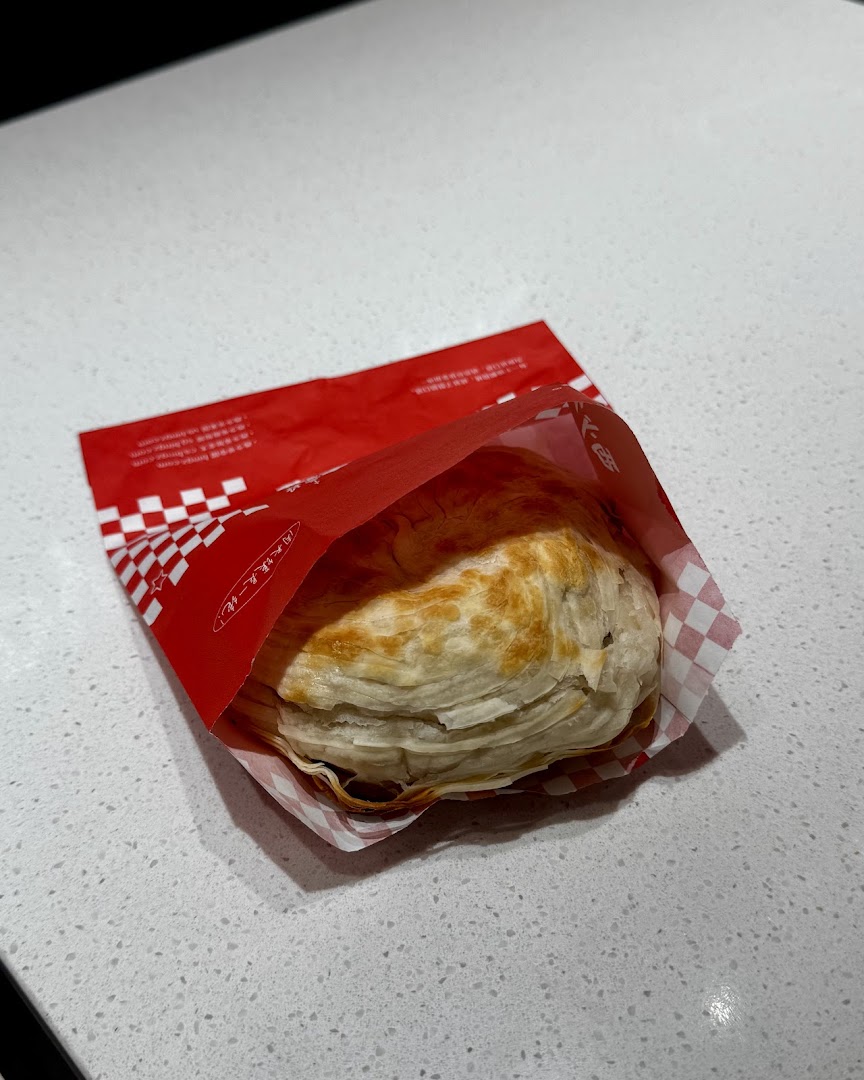 A flaky, golden-brown pastry in a red and white checkered paper sleeve on a white countertop.