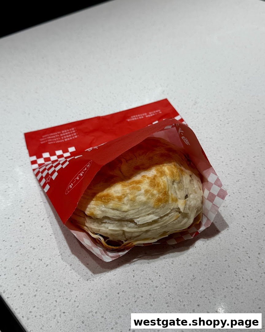 A flaky, golden-brown pastry in a red and white checkered paper sleeve on a white countertop.