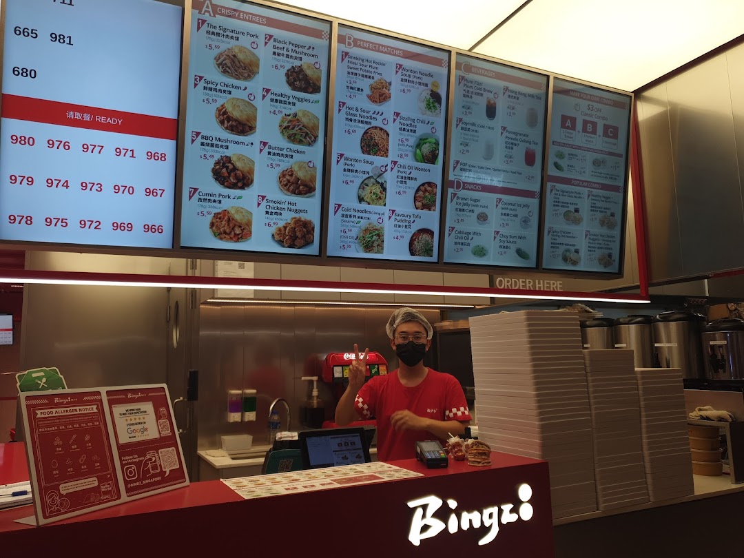 A staff member stands behind the counter with digital menu boards displaying various food and drink options.