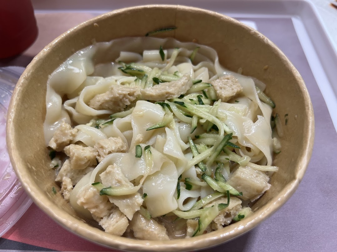 A close-up of a bowl of wide noodles topped with shredded cucumber and a protein, likely from Bingz Singapore.