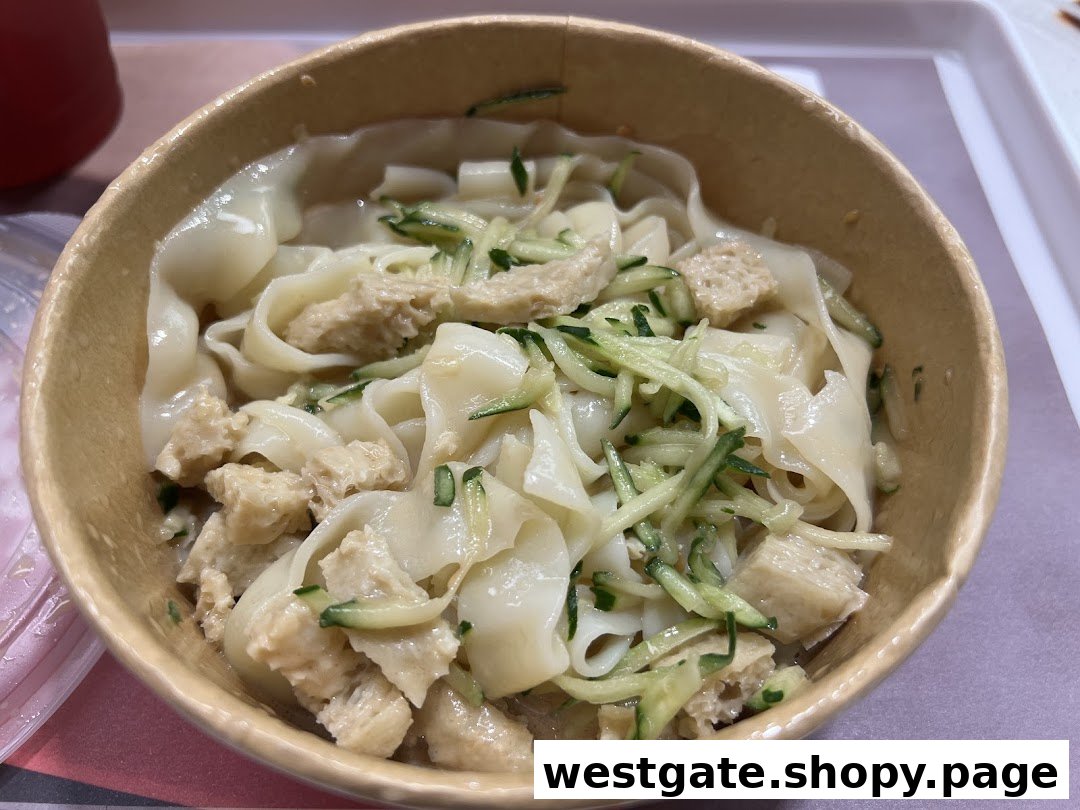 A close-up of a bowl of wide noodles topped with shredded cucumber and a protein, likely from Bingz Singapore.