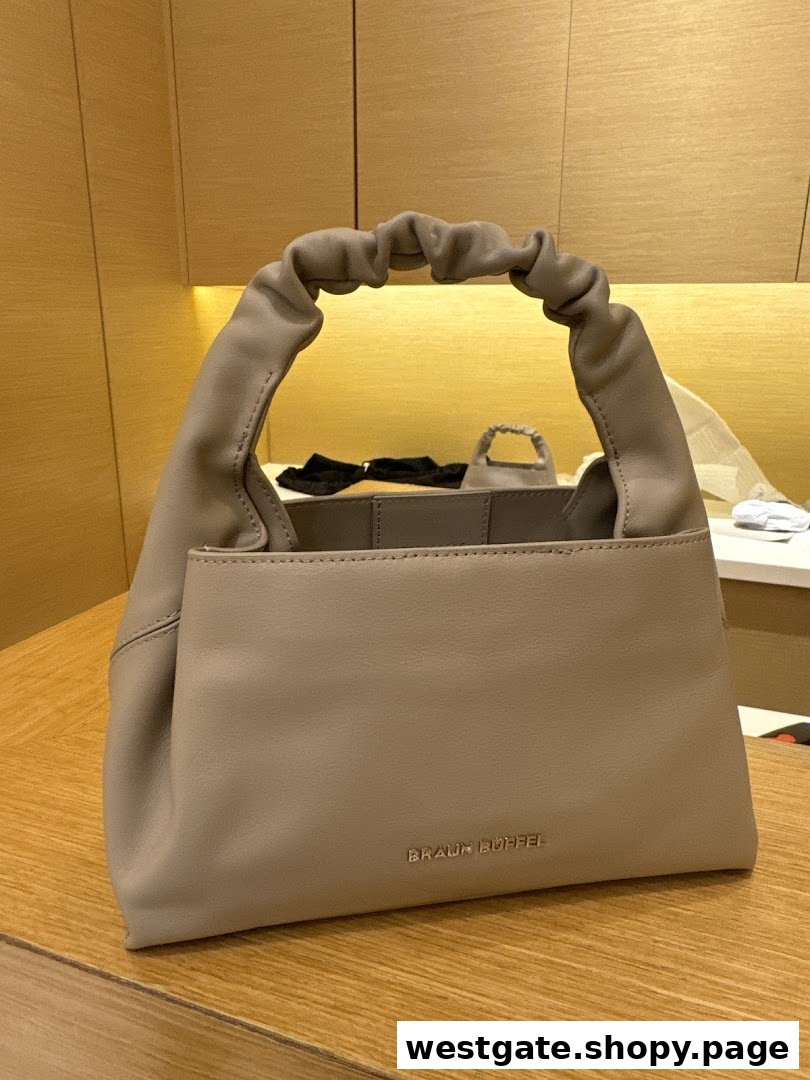 A stylish taupe Braun Büffel handbag with a distinctive ruched handle displayed on a wooden surface.