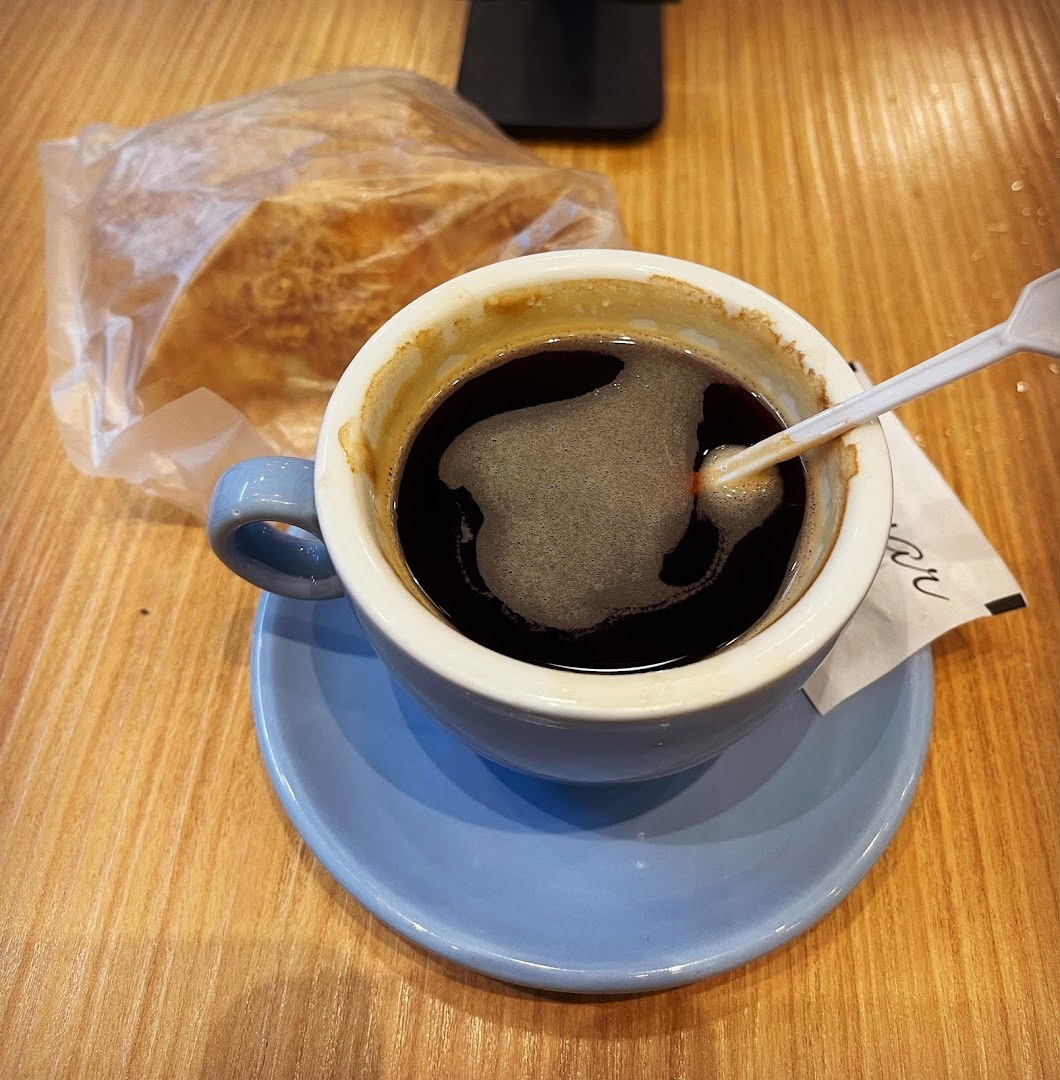A cup of black coffee and a pastry on a wooden table, ready for a delightful break.