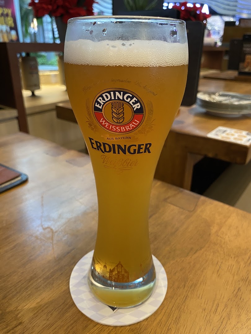 A tall glass of Erdinger Weissbier on a wooden table inside the restaurant.