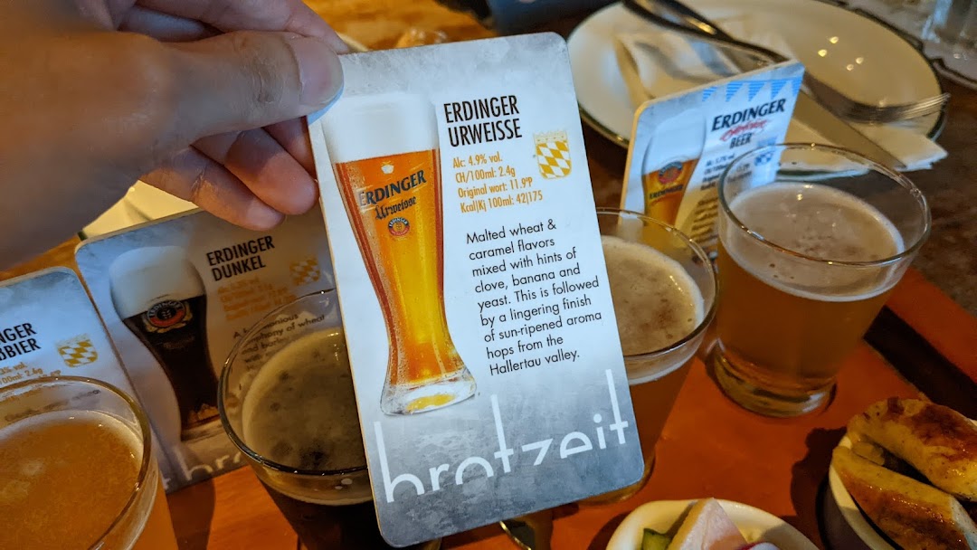 A hand holding a beer information card with several beer glasses and food on a table.