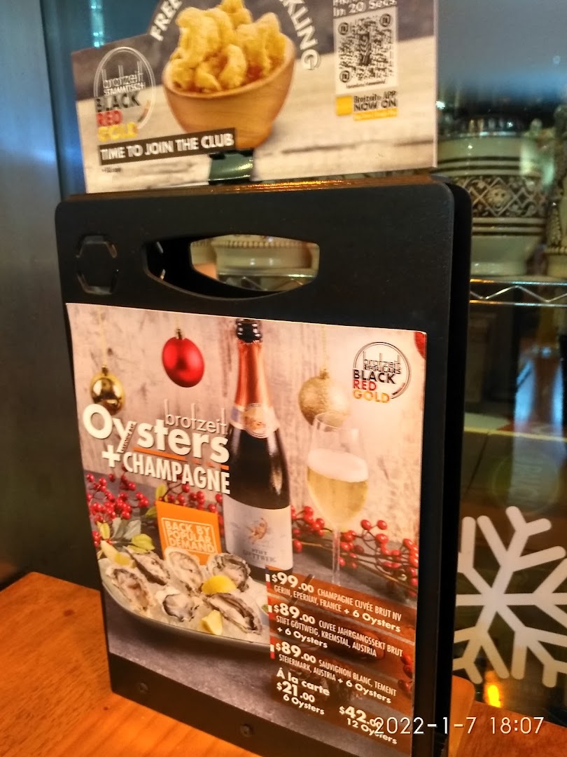 A table stand displaying Brotzeit's Oysters + Champagne promotion with prices and club membership details.