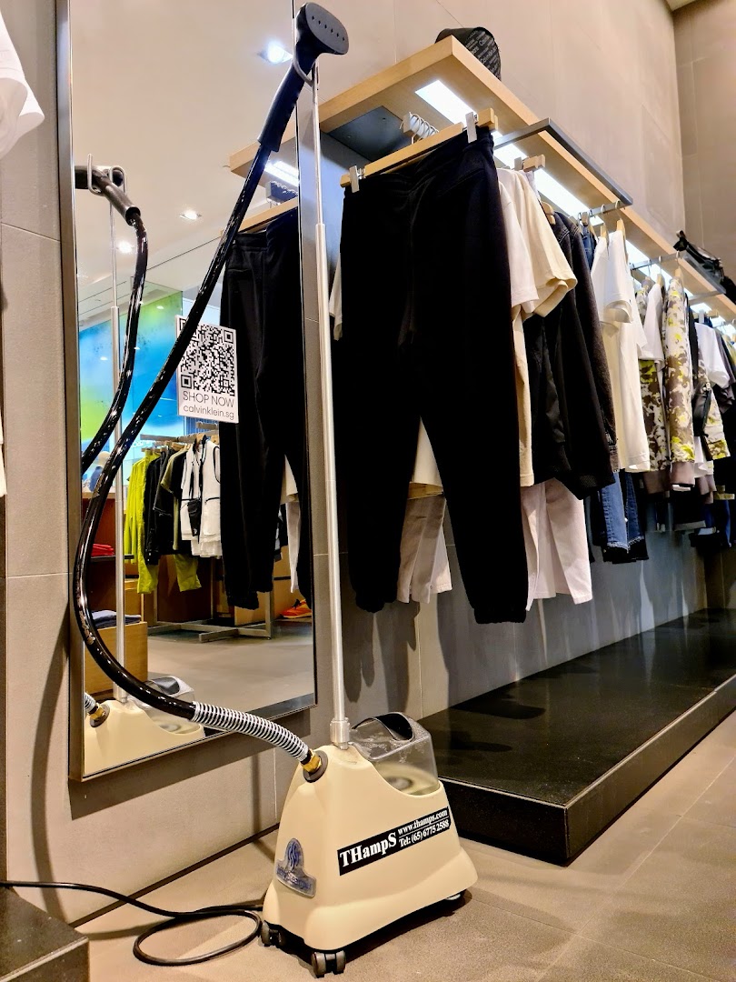 An interior view of a Calvin Klein store showcasing clothing racks, a mirror, and a garment steamer.