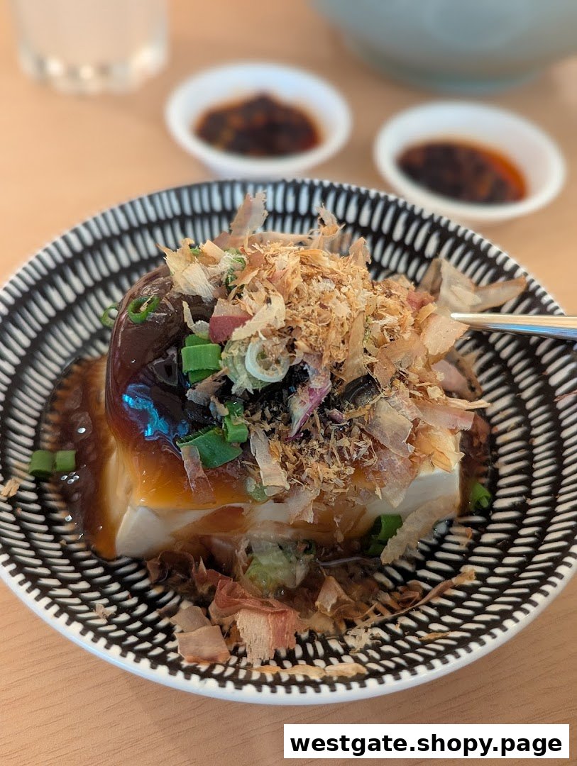 A close-up of a delicious tofu dish topped with bonito flakes, spring onions, and a savory sauce.