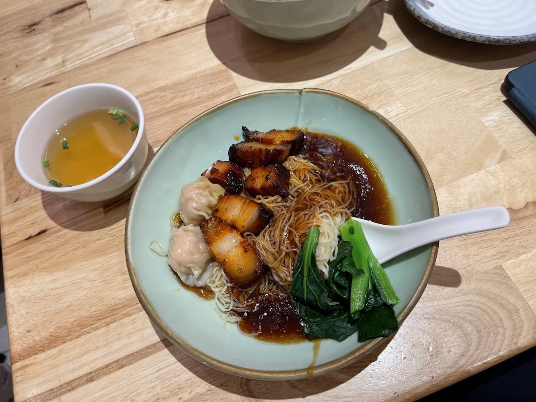 A delicious bowl of wanton noodles with char siew and vegetables, served with a side of soup.