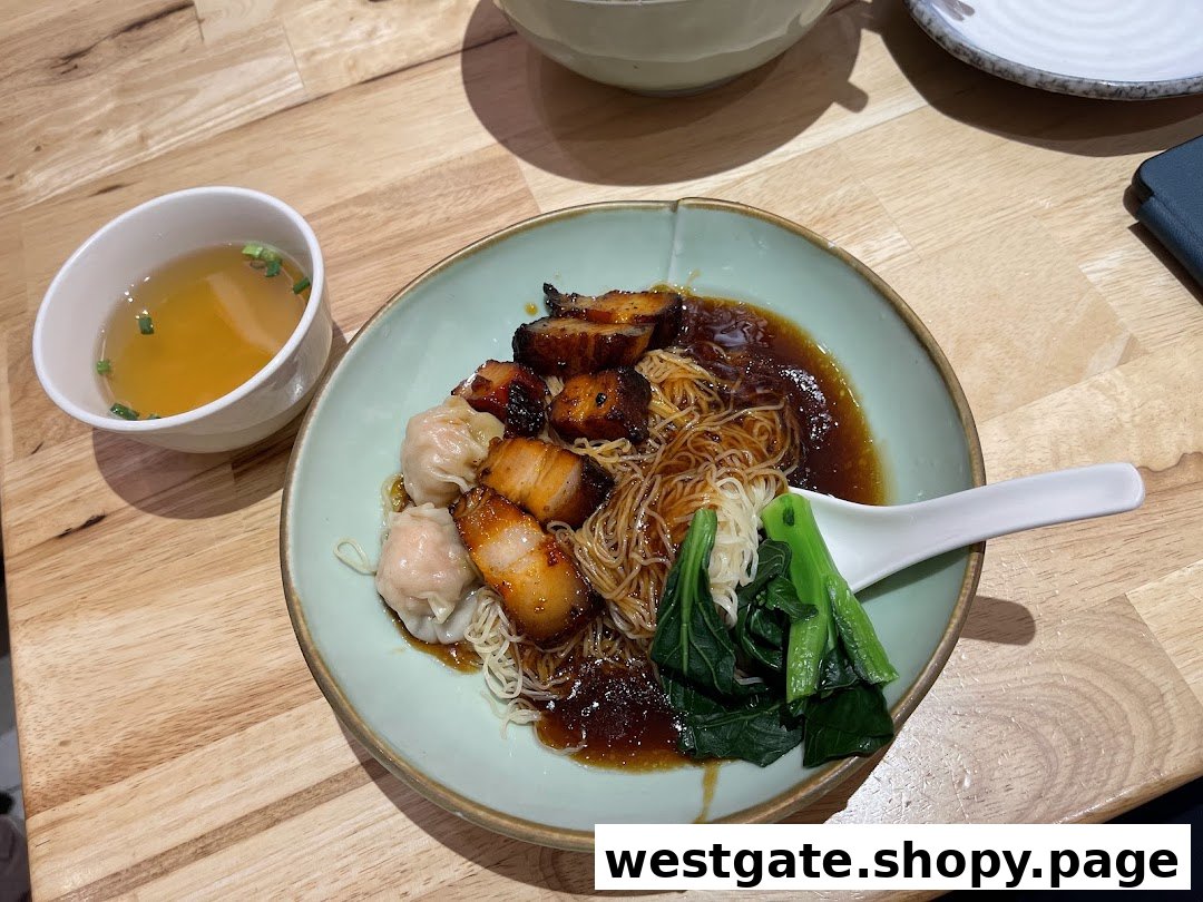 A delicious bowl of wanton noodles with char siew and vegetables, served with a side of soup.