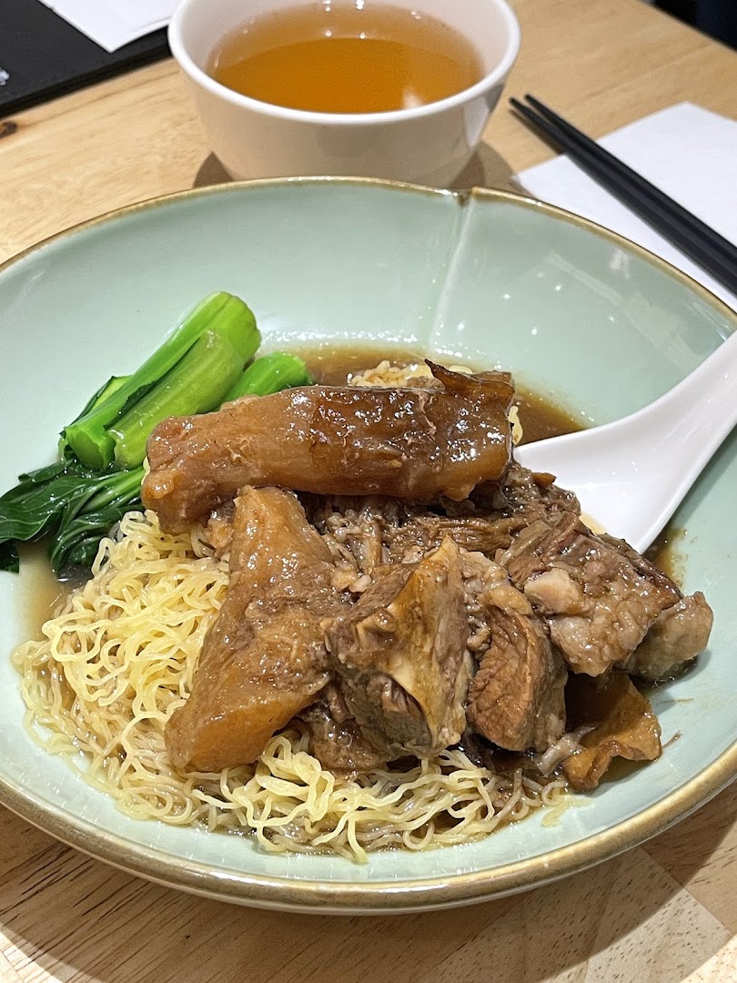 A close-up of a delicious bowl of braised beef brisket noodles with green vegetables and a side of tea.