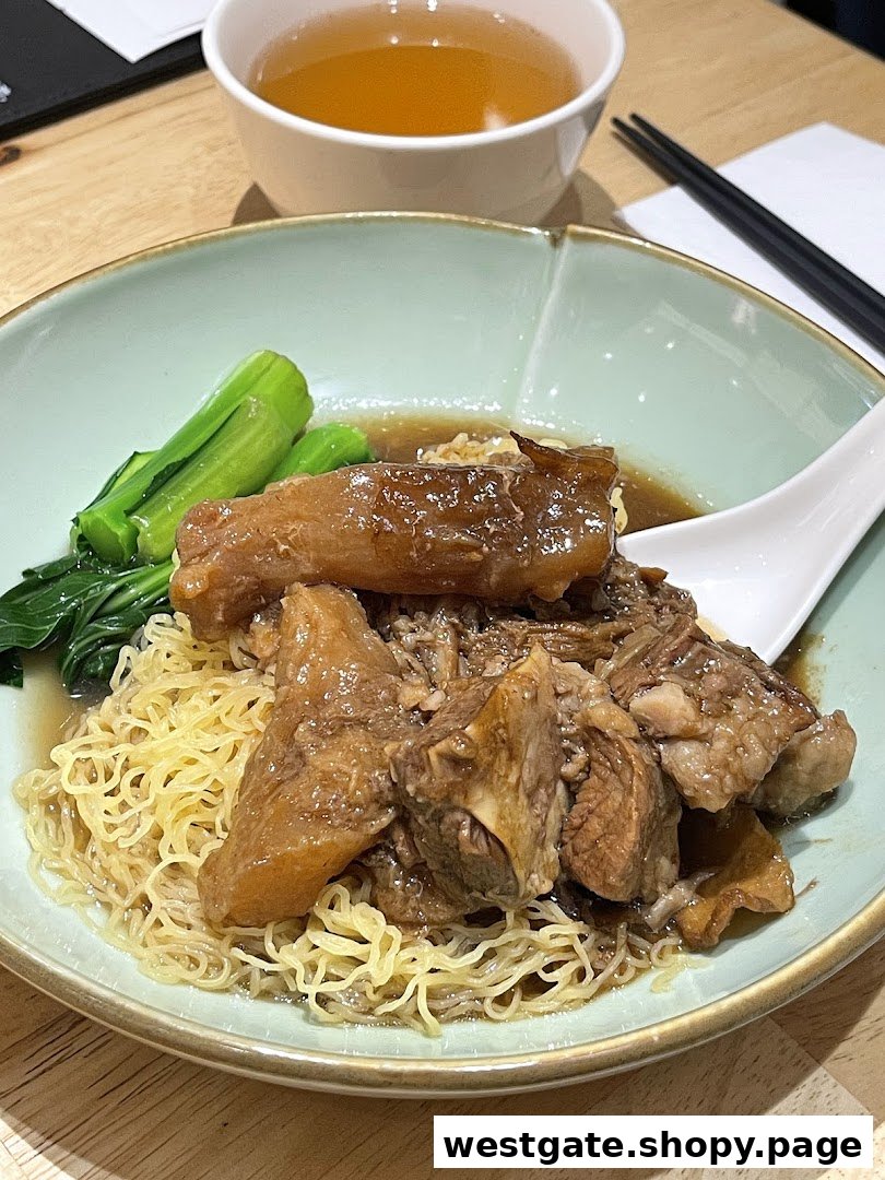 A close-up of a delicious bowl of braised beef brisket noodles with green vegetables and a side of tea.