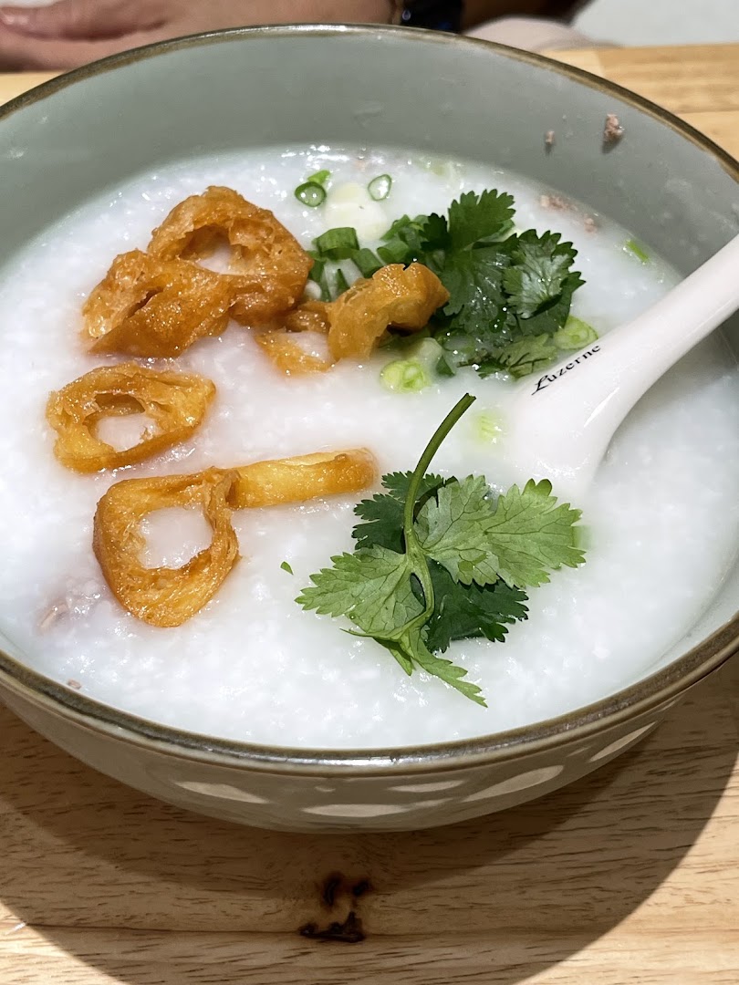 A close-up of a bowl of congee topped with fried dough fritters, spring onions, and fresh coriander.