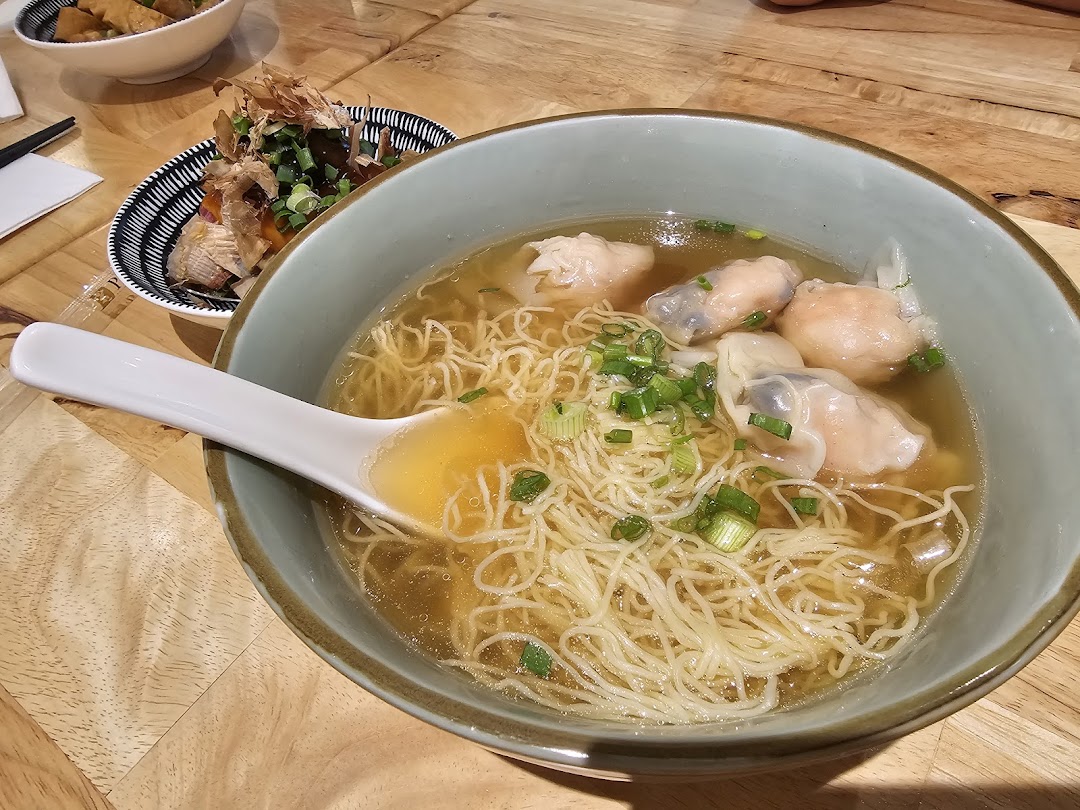 A close-up of a delicious bowl of wanton noodles with a side dish on a wooden table.