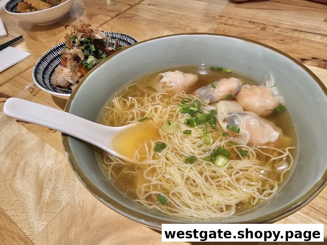 A close-up of a delicious bowl of wanton noodles with a side dish on a wooden table.