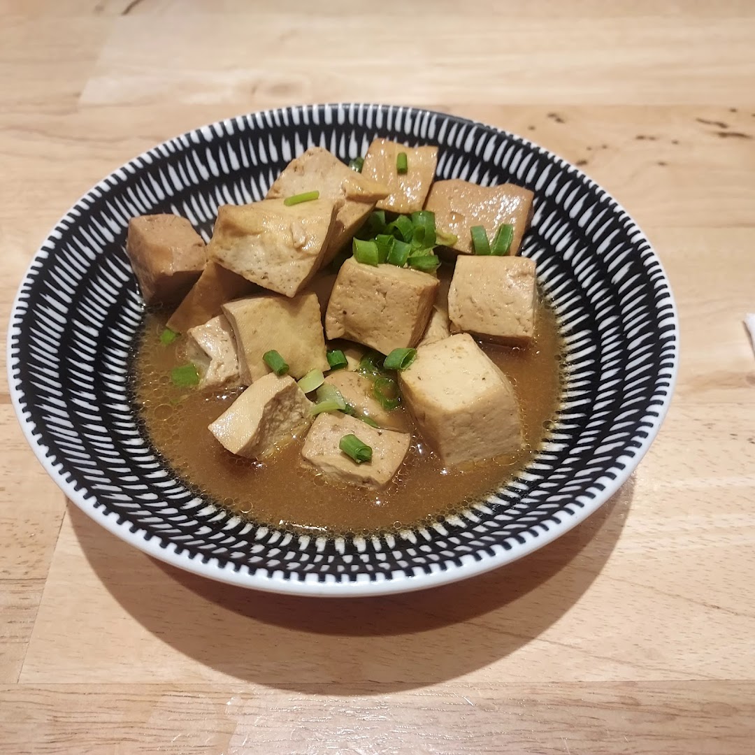 A close-up of a bowl of braised tofu garnished with chopped spring onions.