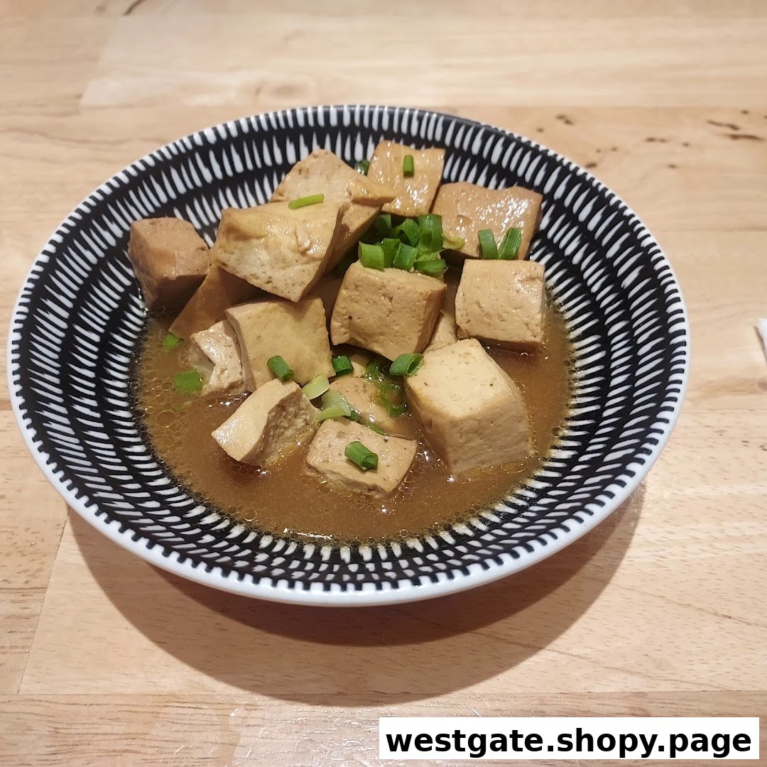 A close-up of a bowl of braised tofu garnished with chopped spring onions.
