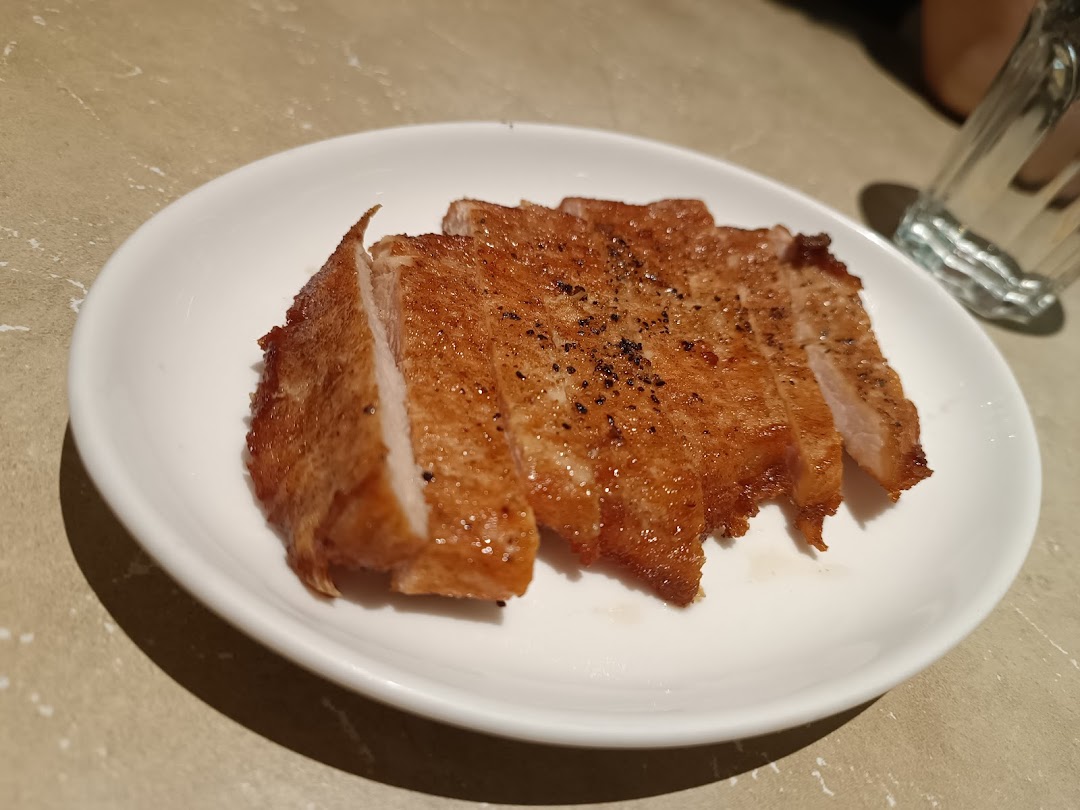 A plate of perfectly fried and sliced pork chop, seasoned with black pepper.