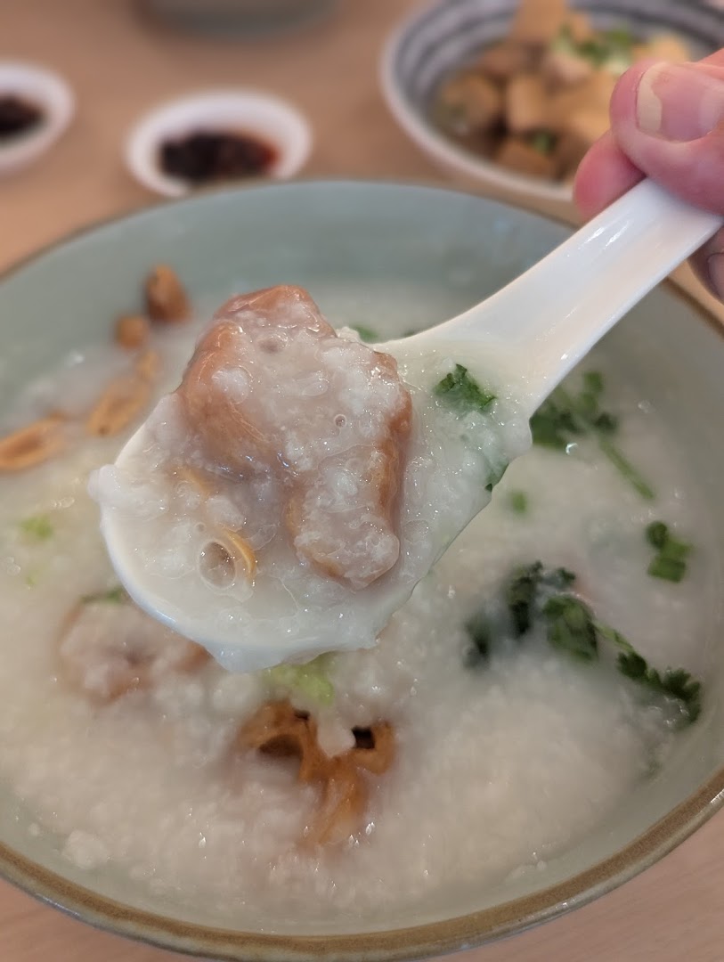 A close-up shot of a spoon lifting a spoonful of comforting congee with ingredients from a bowl.