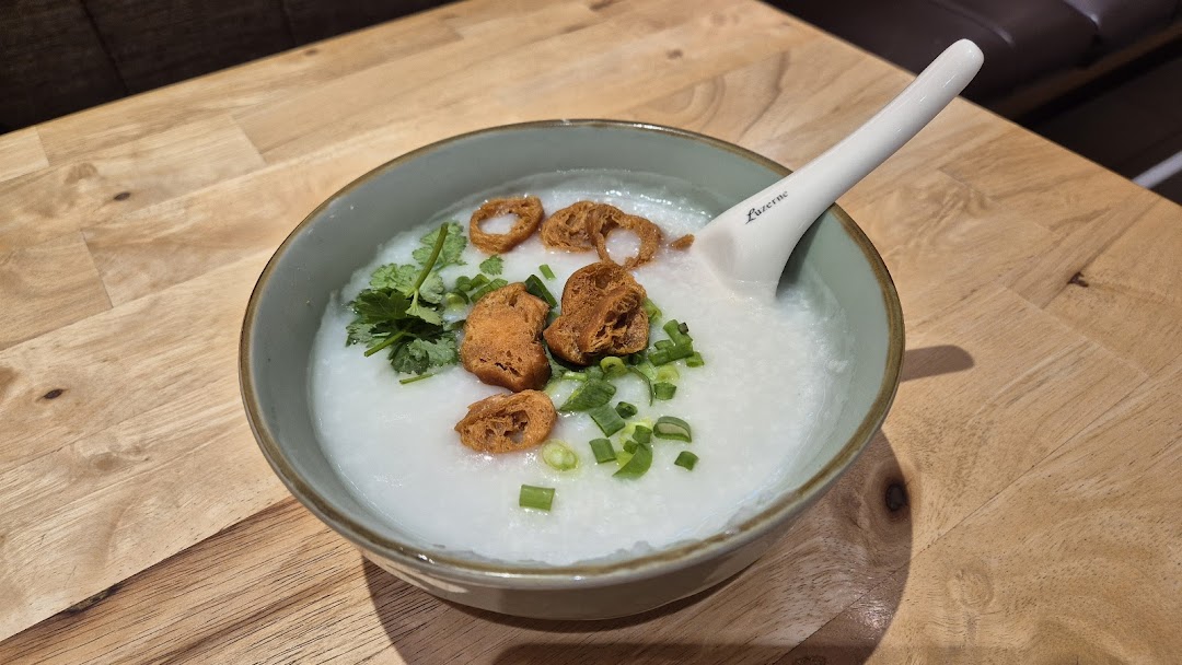 A comforting bowl of congee topped with fried dough, spring onions, and cilantro on a wooden table.