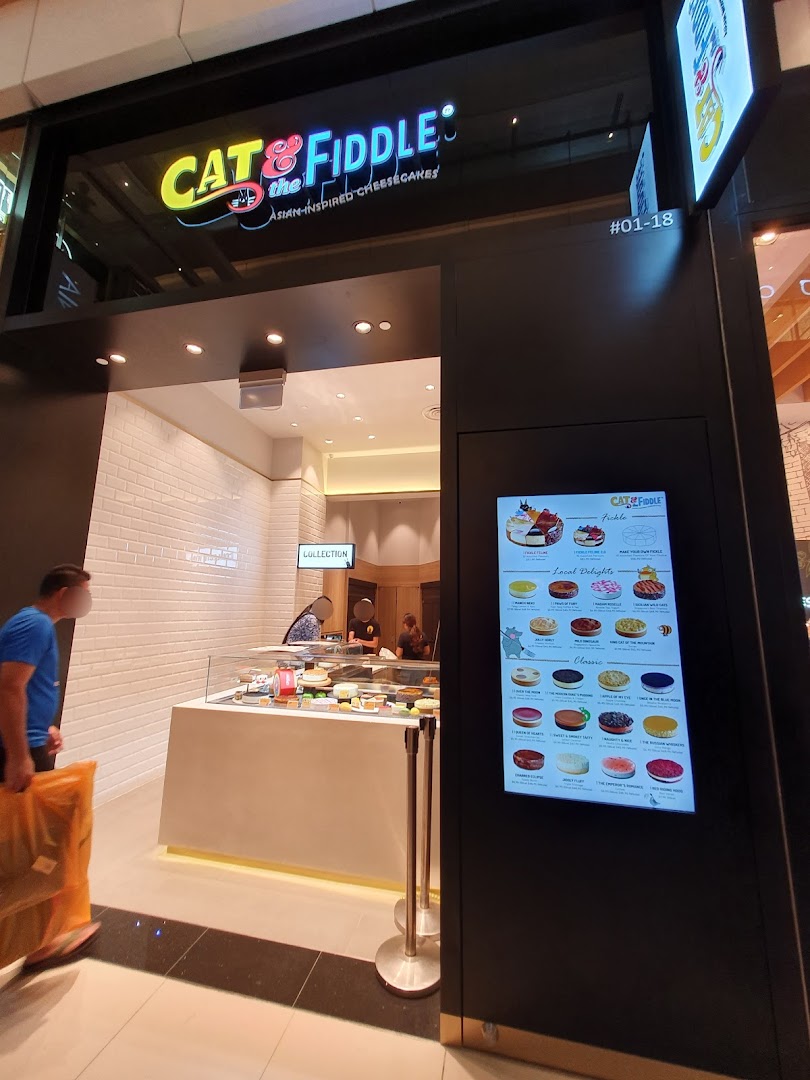 The shopfront of Cat & the Fiddle Cakes, featuring its logo, display counter, and a digital menu board.