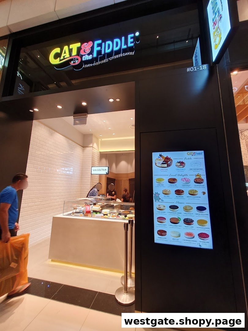 The shopfront of Cat & the Fiddle Cakes, featuring its logo, display counter, and a digital menu board.