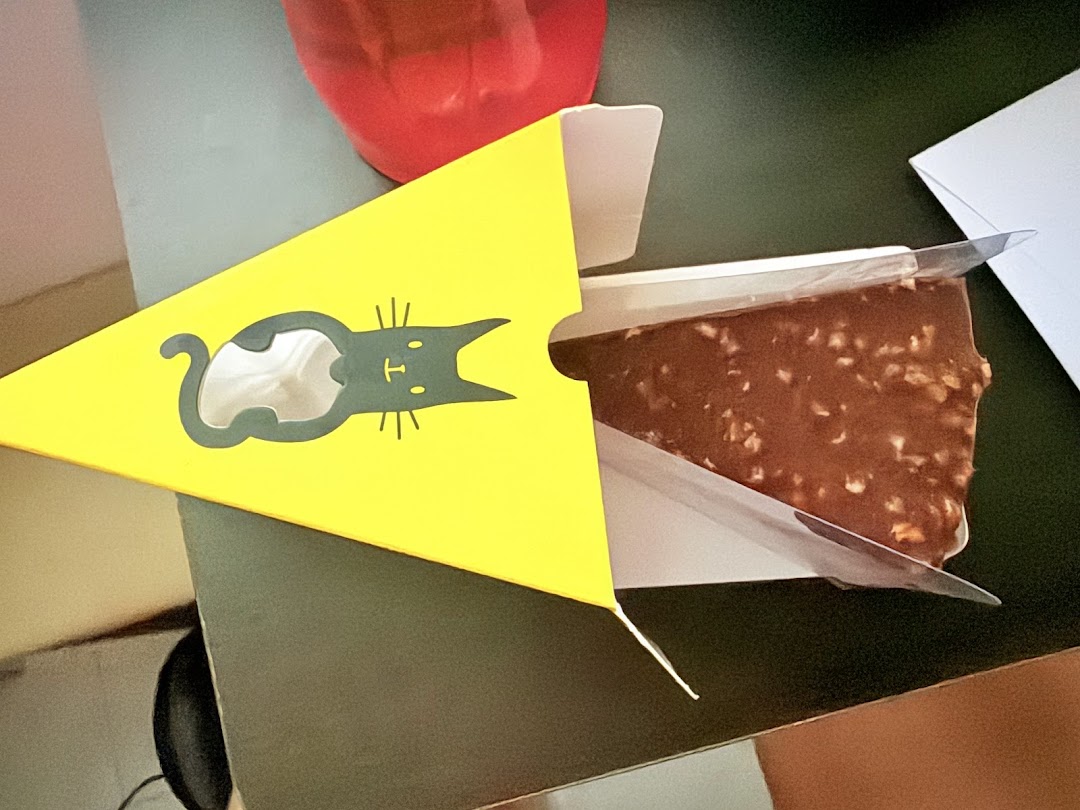 A delicious chocolate cake slice with nuts, presented in a distinctive yellow box with a cat logo.