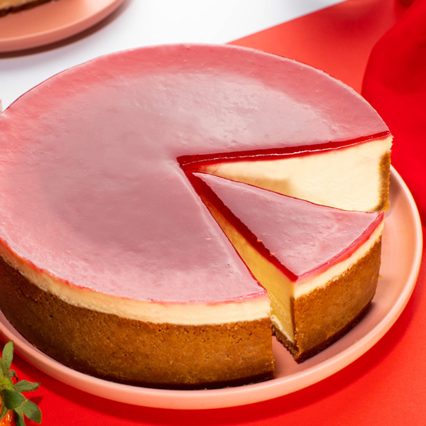 A delicious cheesecake with a slice removed, featuring a pink glaze and creamy filling.