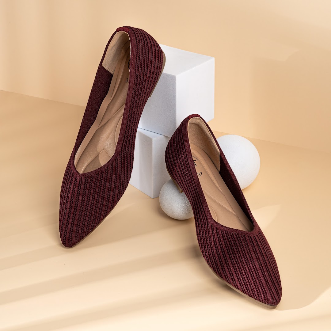 A pair of stylish maroon knitted ballet flats displayed on a light background with white geometric props.