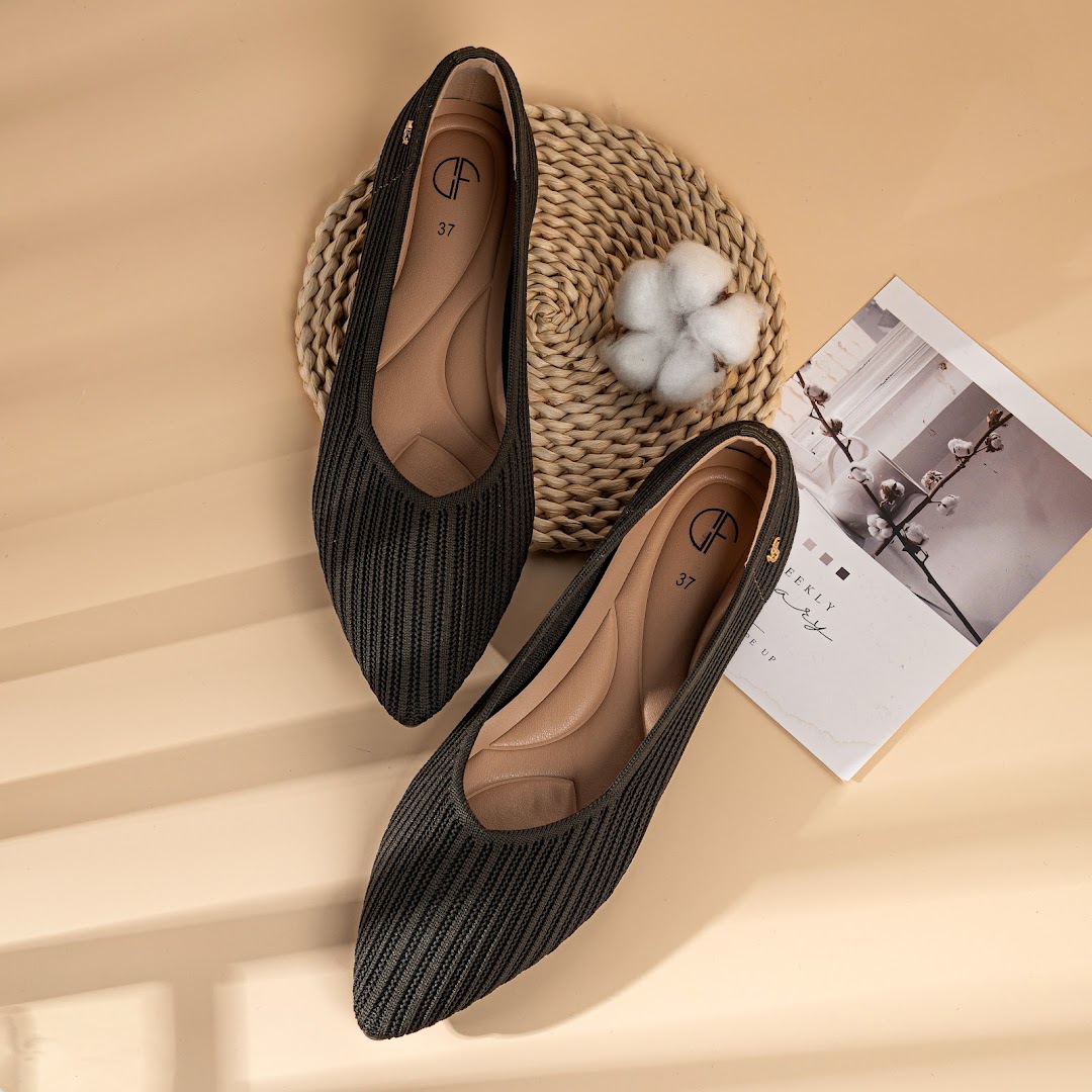 A pair of dark green knitted ballet flats with cushioned insoles, displayed on a beige surface.