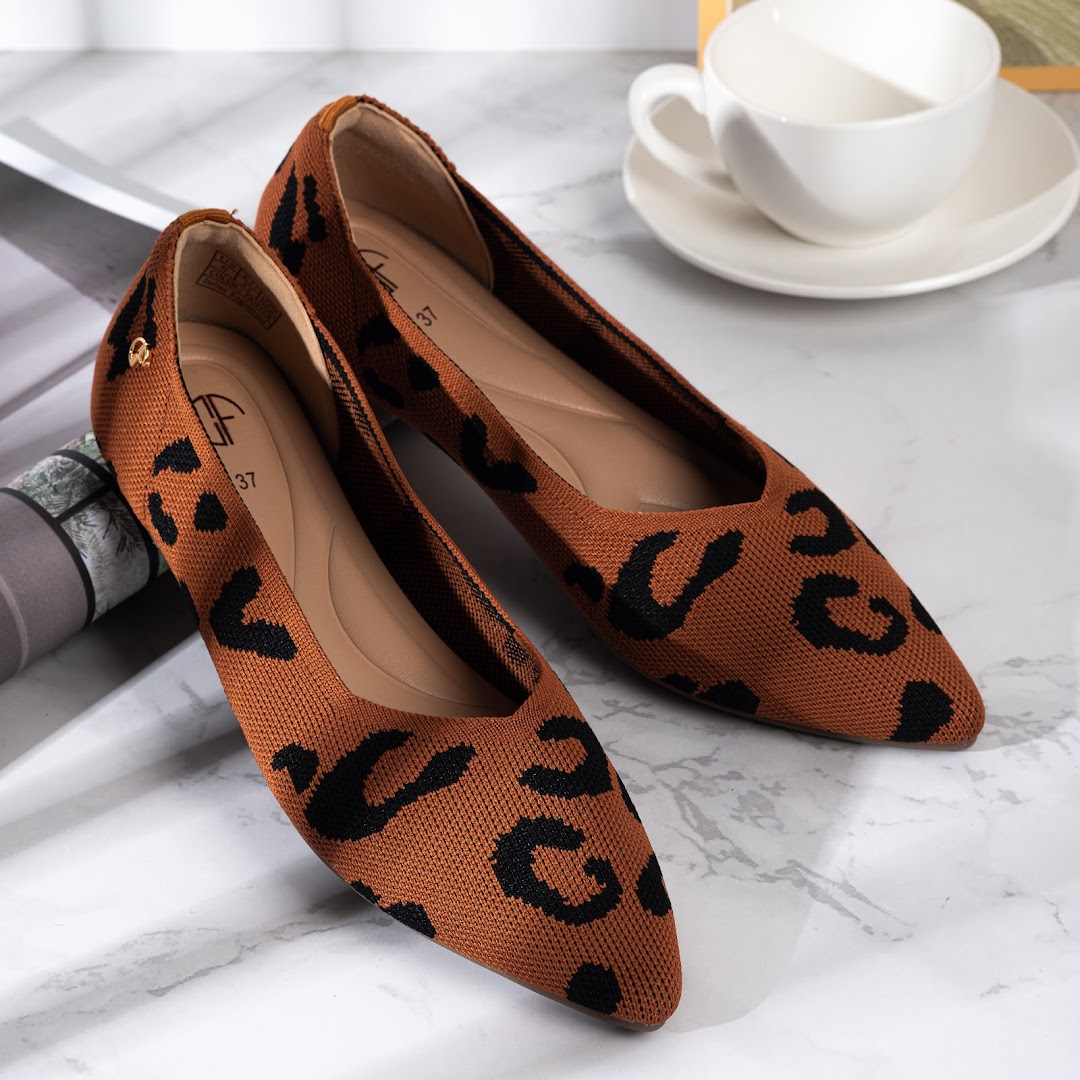 A pair of stylish brown and black leopard print flat shoes displayed on a marble surface.