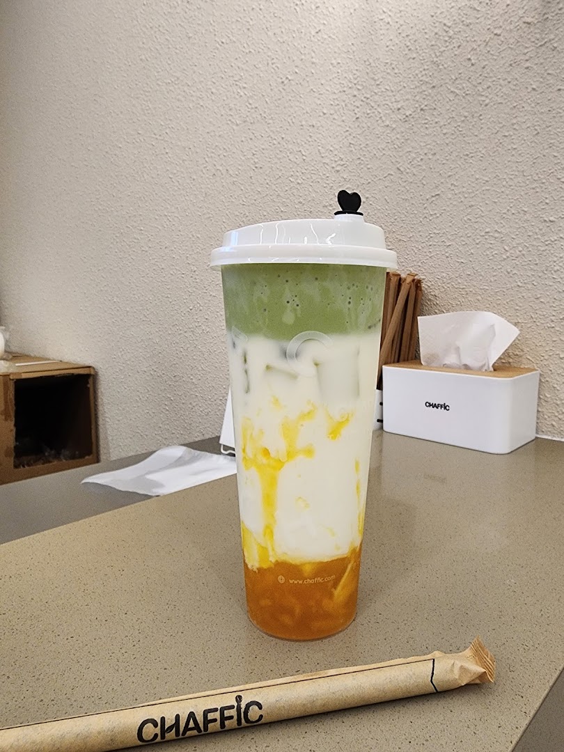 A vibrant, layered beverage from Chaffic, featuring green, white, and orange hues, on a counter.