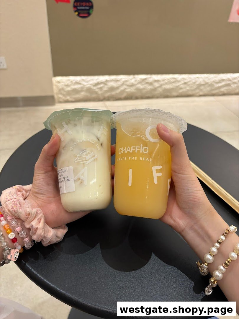Two hands hold refreshing Chaffic beverages, one milk tea and one fruit drink, over a black table.