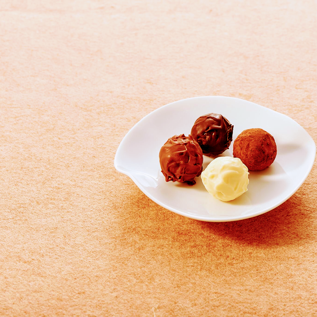 Four delicious chocolate truffles, including dark, milk, and white chocolate, presented on a white plate.