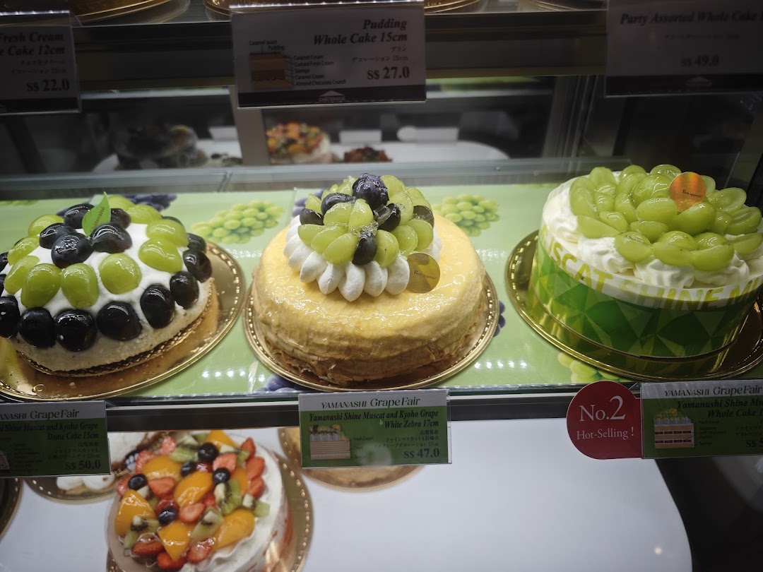 A vibrant display of fresh fruit cakes, including grape-themed desserts, in a chilled showcase.