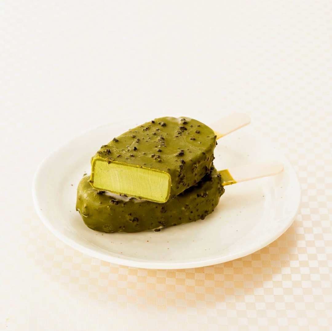 Two matcha ice cream bars, one cut open to reveal the green interior, are displayed on a white plate.