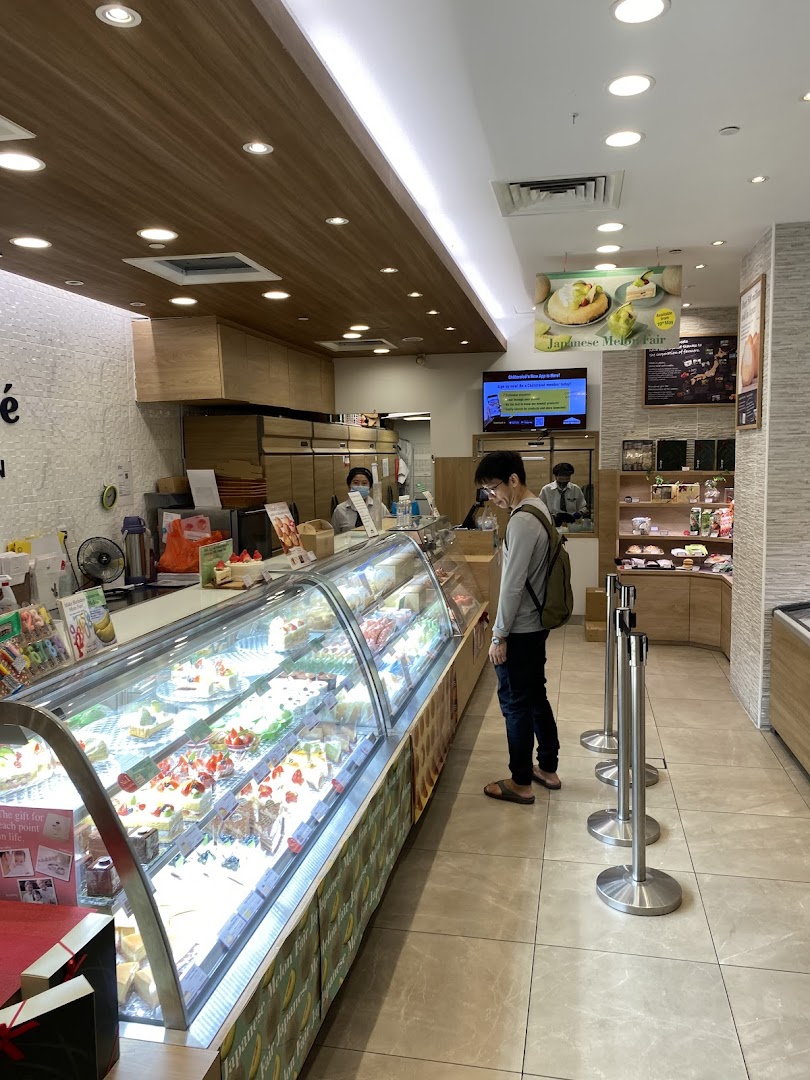 A customer browses a brightly lit display case filled with various cakes and pastries inside a Châteraisé store.