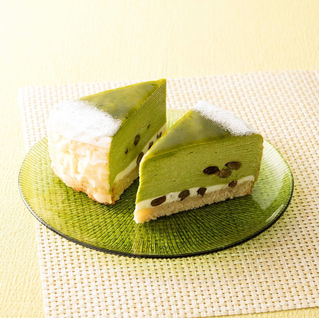 Two slices of vibrant green matcha cake with red beans and cream on a green glass plate.