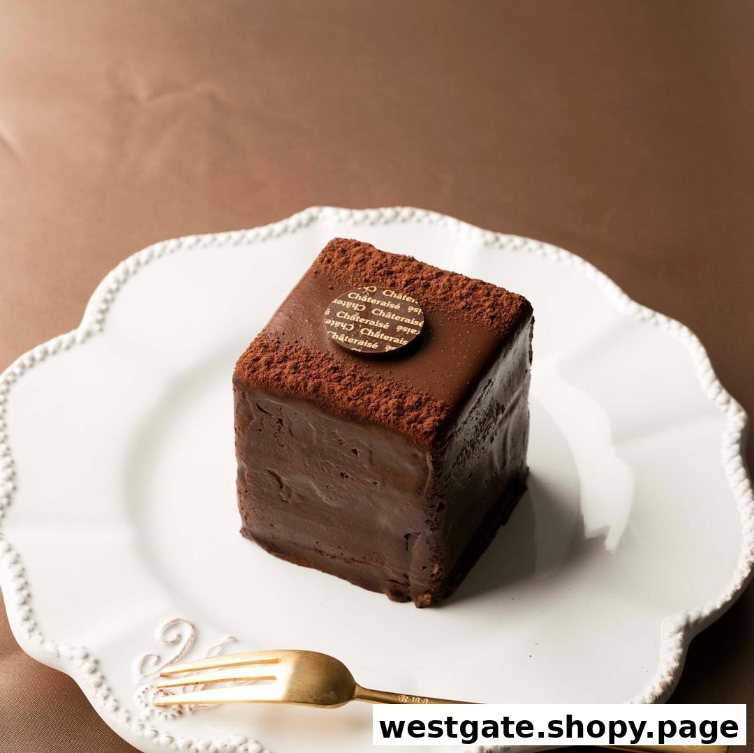 A rich, square chocolate cake with cocoa powder and a Châteraisé logo on a white plate with a gold fork.