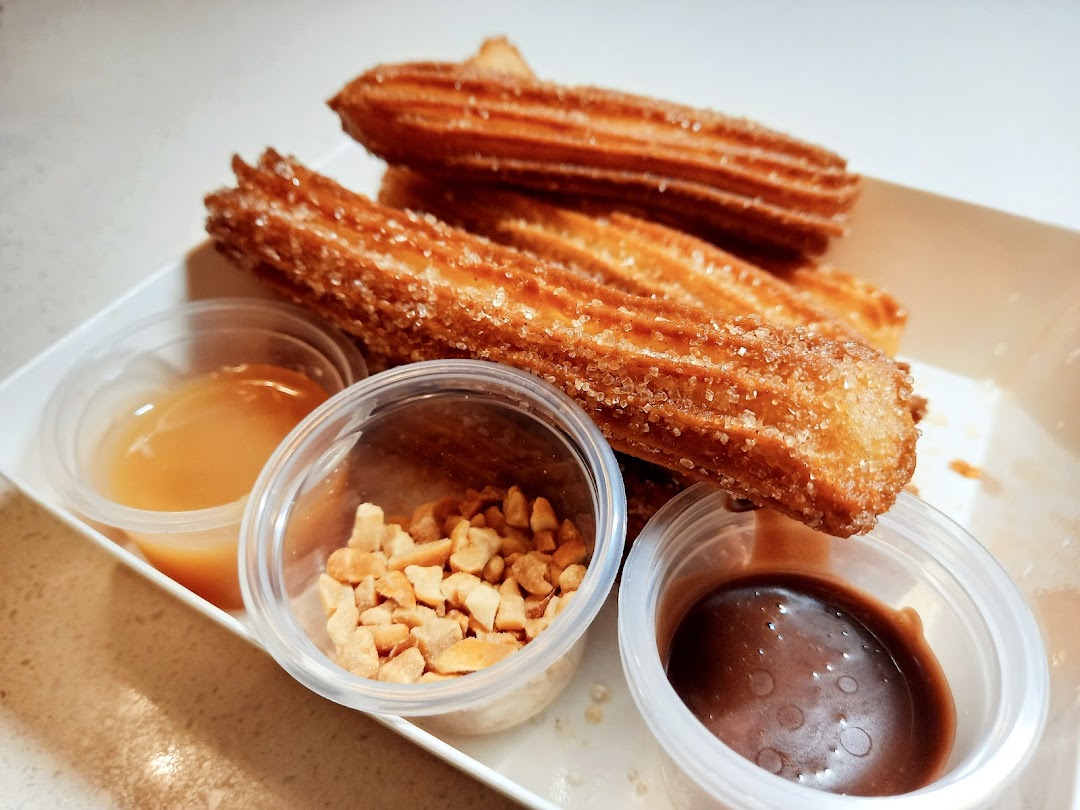 A plate of golden churros dusted with sugar, served with caramel, chocolate, and nut dips.
