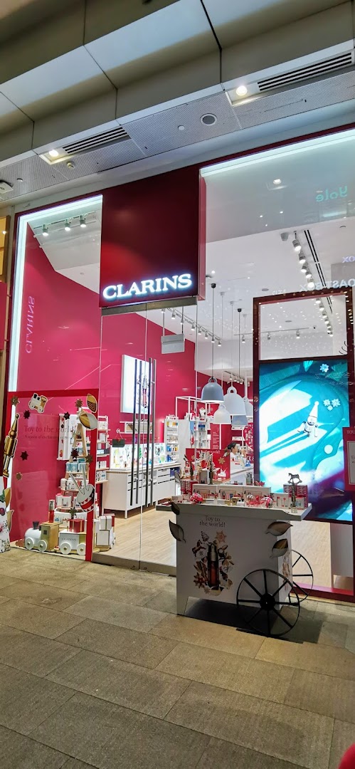 The Clarins boutique entrance features vibrant pink decor and festive holiday displays.