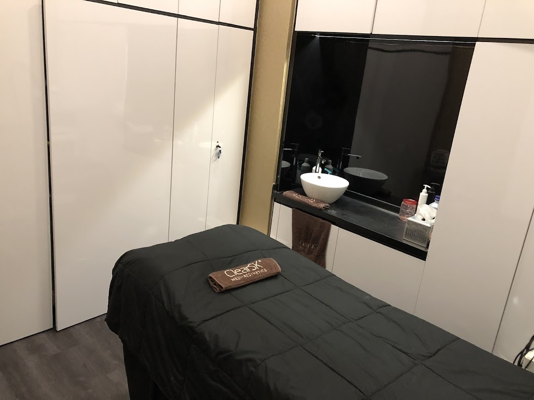 An aesthetic clinic treatment room featuring a comfortable bed and a modern sink area.