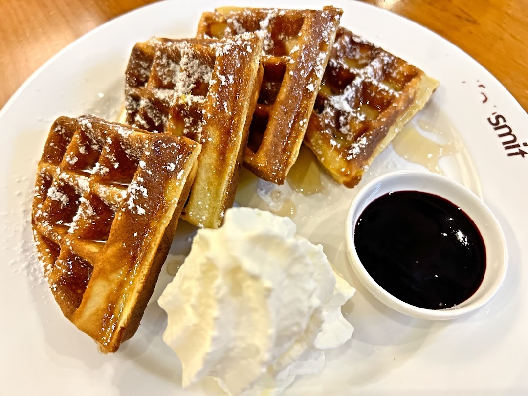 Golden waffles with powdered sugar, whipped cream, and berry sauce on a white plate.