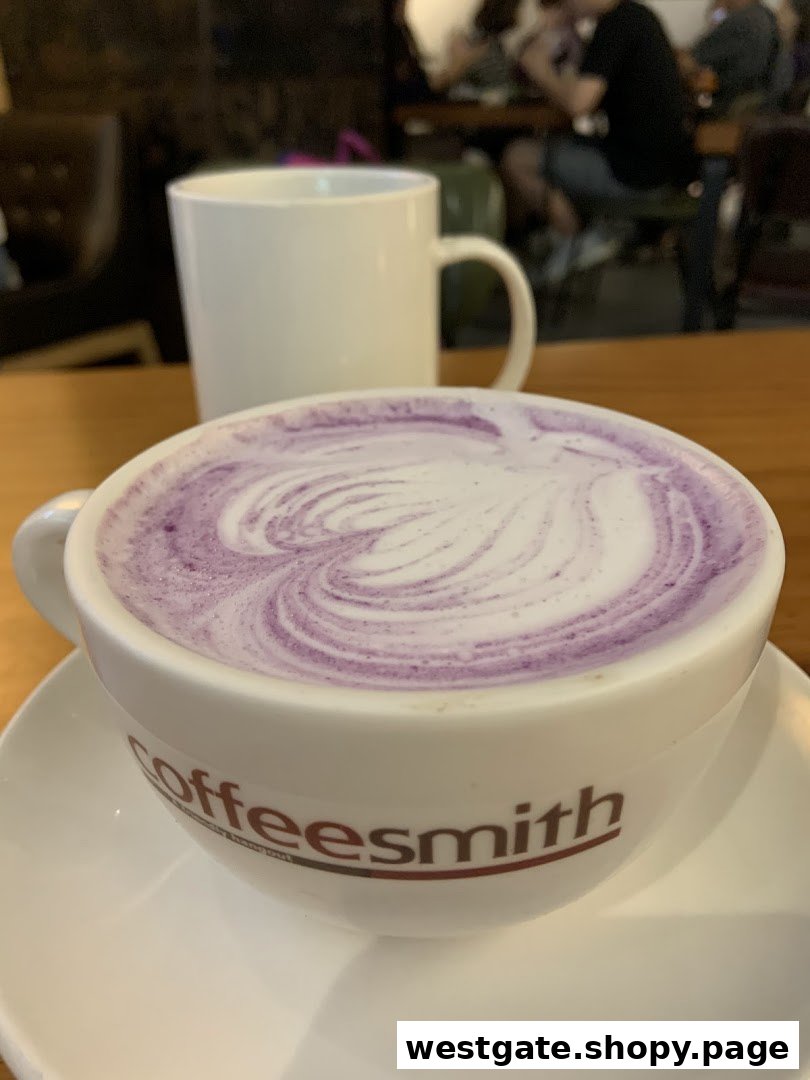 A close-up of a purple latte with latte art in a Coffeesmith cup, with a blurred interior background.