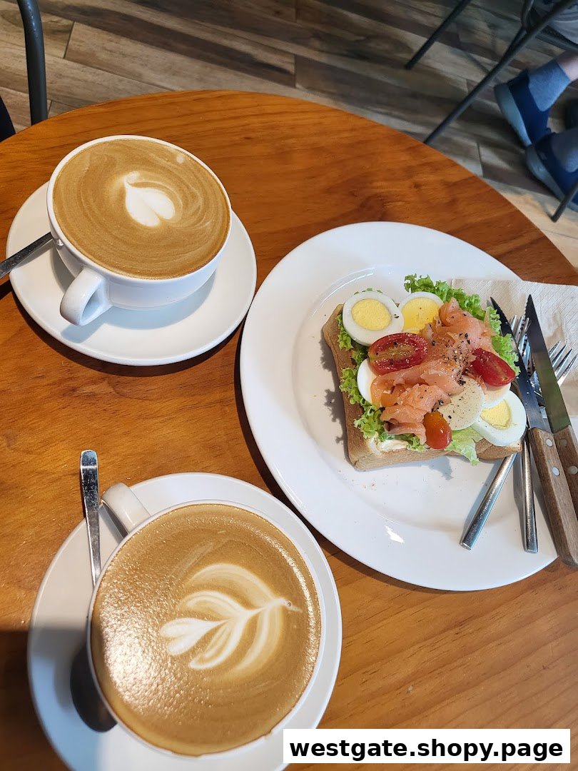 Two lattes with latte art and a savory toast with salmon and eggs on a wooden table.