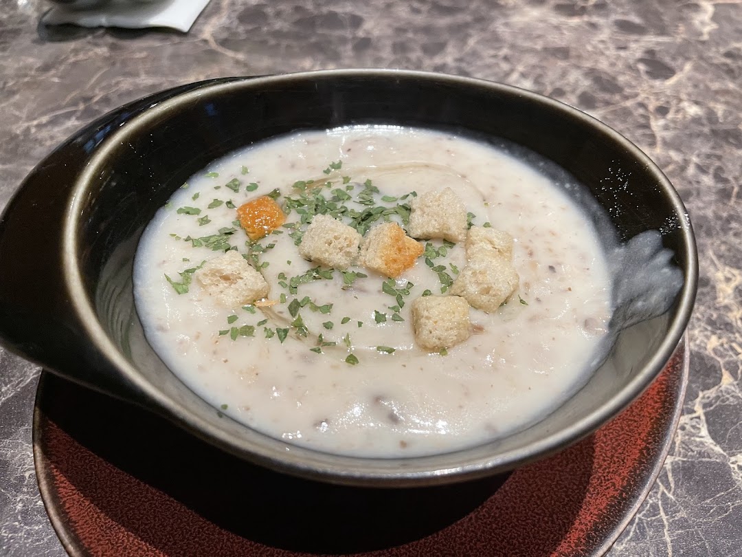A creamy mushroom soup topped with croutons and fresh herbs in a dark bowl.