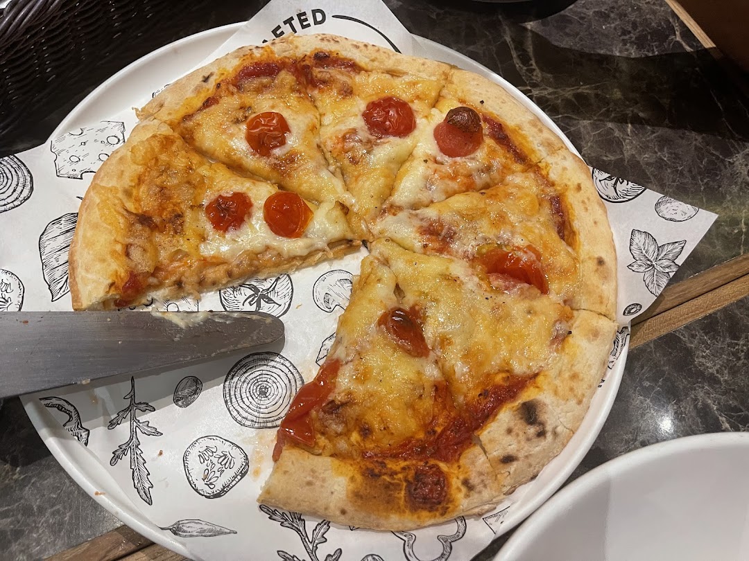 A delicious cheese and tomato pizza with cherry tomatoes, served on a patterned paper liner.