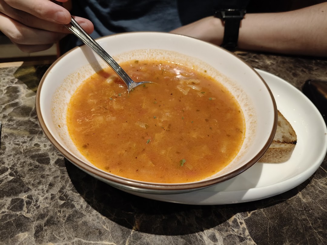 A close-up of a hearty bowl of tomato-based soup with a spoon and a side of bread.
