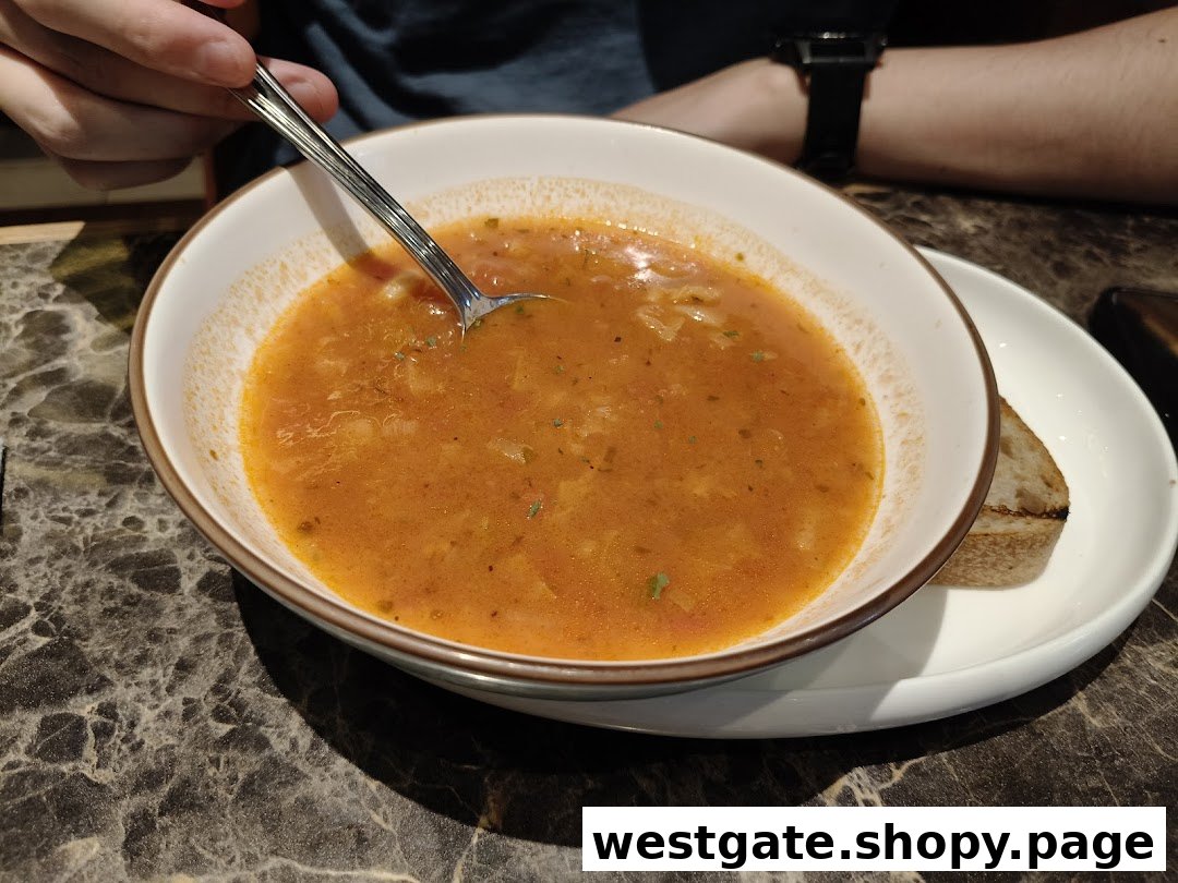 A close-up of a hearty bowl of tomato-based soup with a spoon and a side of bread.